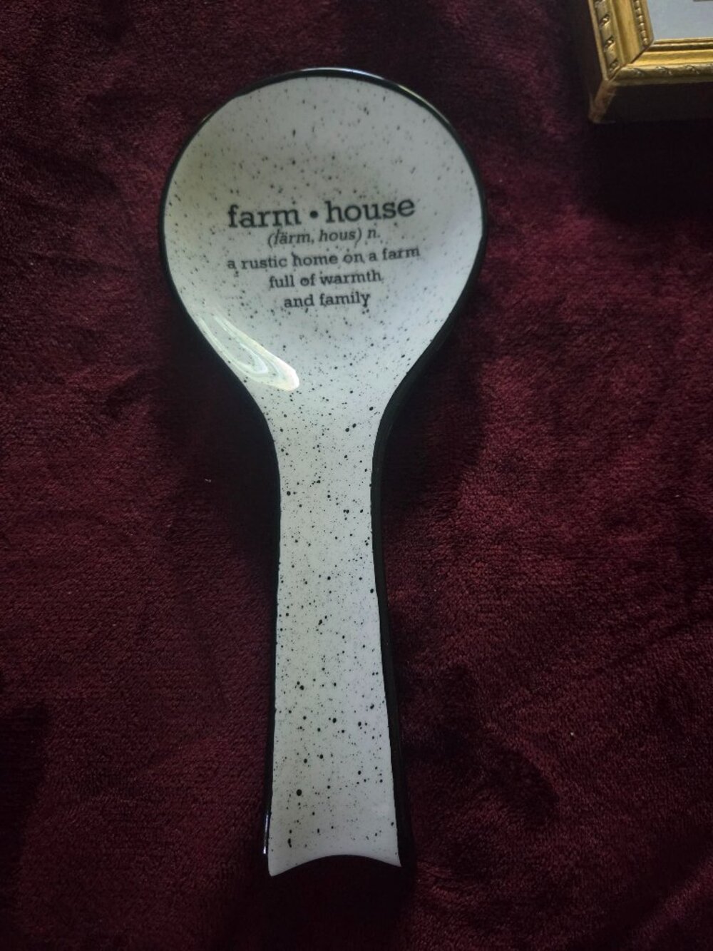 white and black speckled ceramic spoon rest featuring a definition of farmhouse
